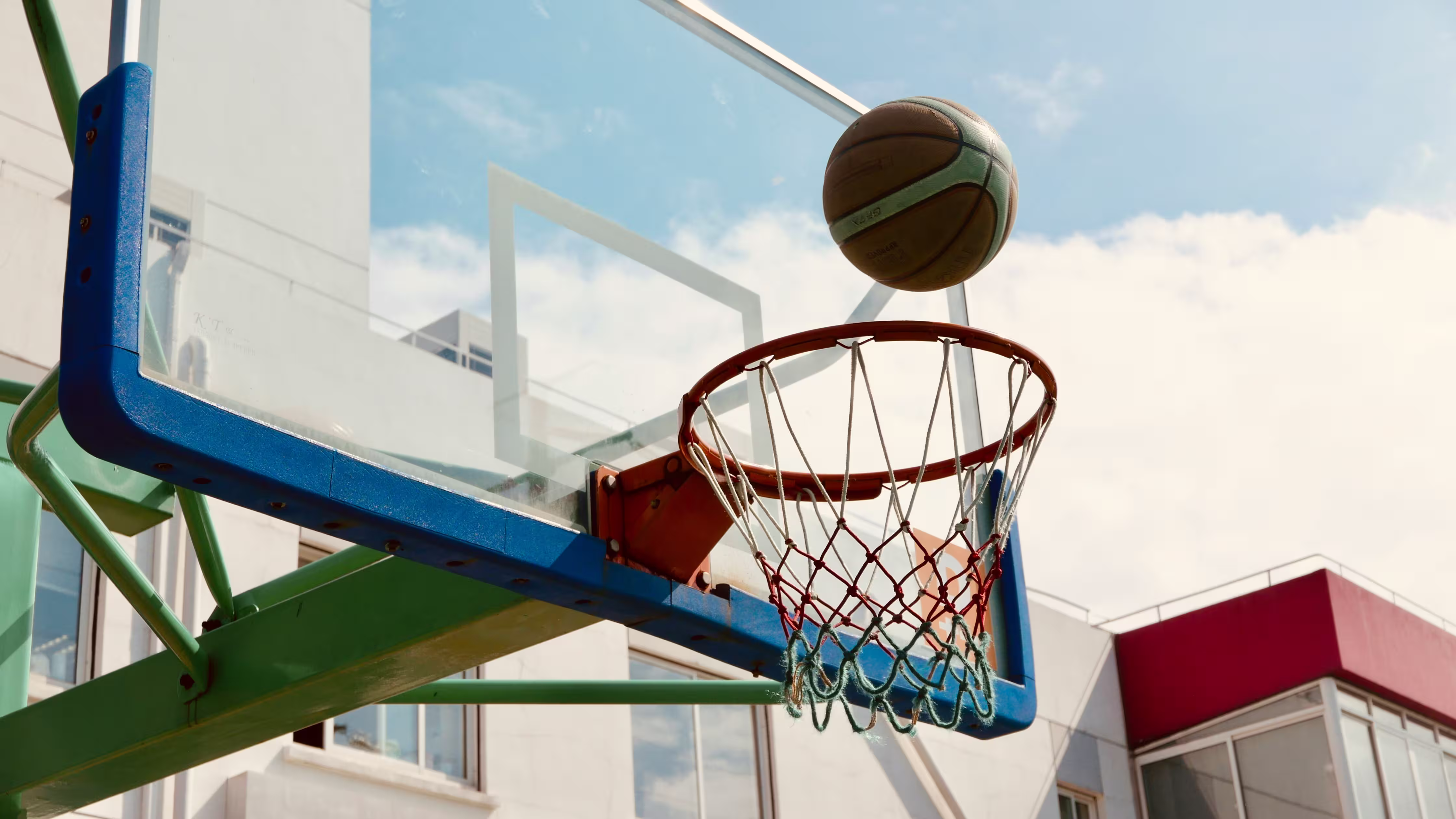 Technician repairing an in-ground basketball hoop, tightening bolts on an outdoor court to ensure stability and safety.