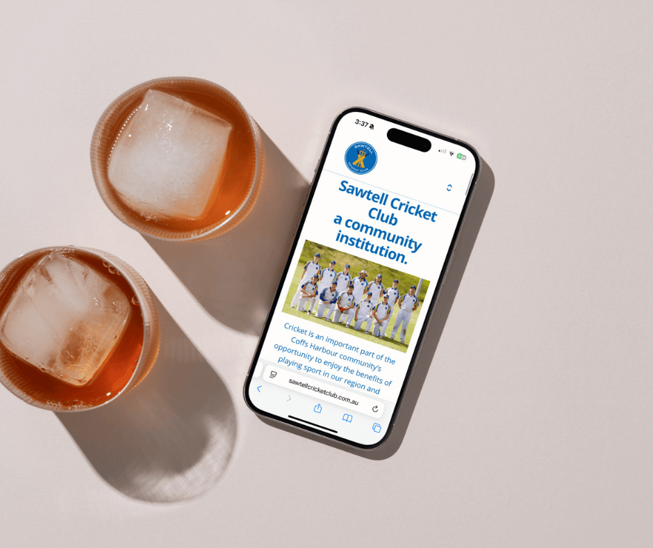 Home page of the Sawtell Cricket Club on a phone on a table with two drinks beside it