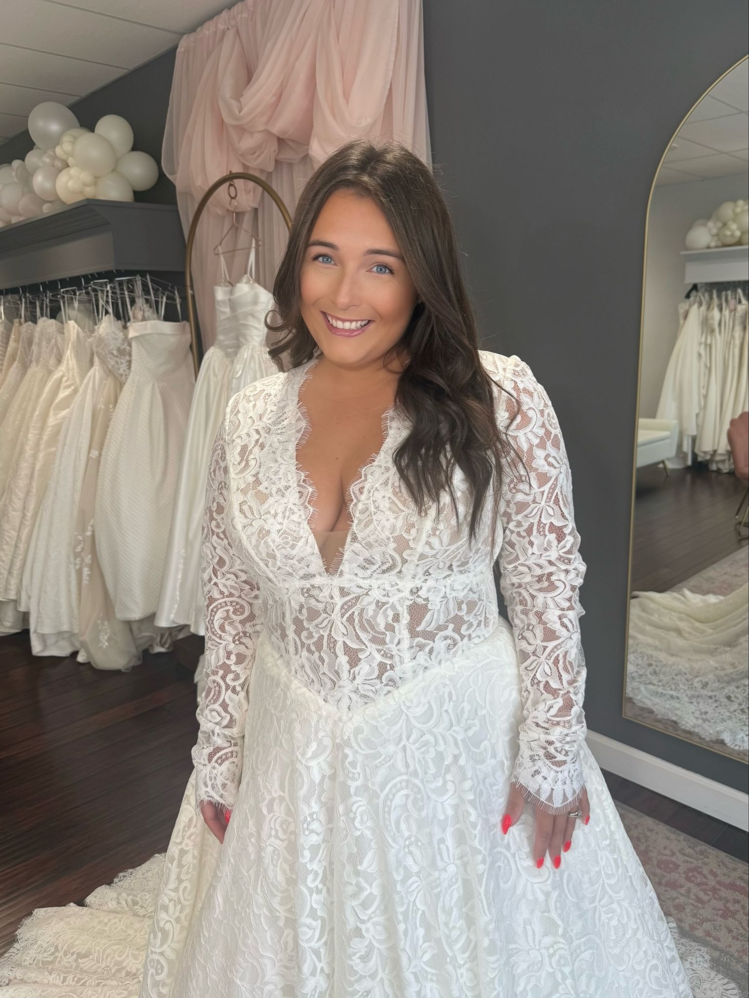 Smiling model in a long-sleeve lace wedding dress with a plunging V-neck, a plus-size bridal look at Blush Bridal