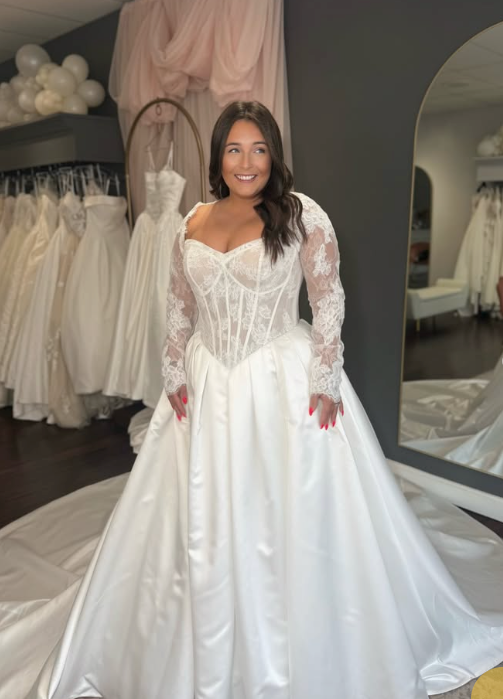 Model in a ball gown wedding dress with a sheer lace corset bodice, long lace sleeves and a full satin skirt