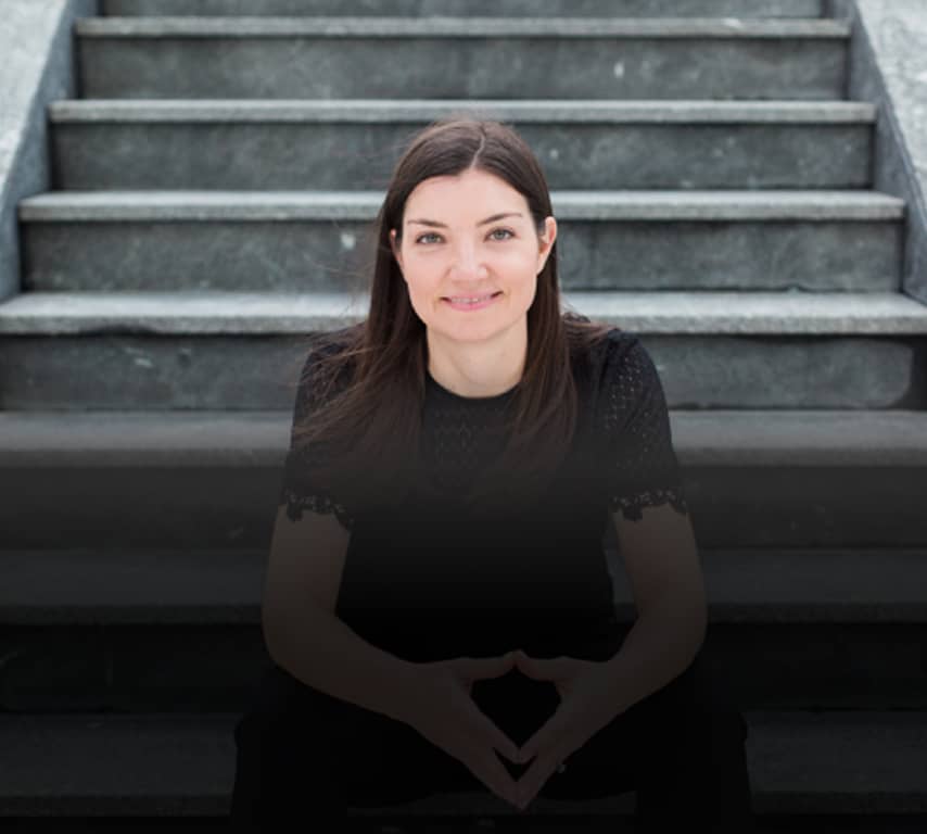 Olivia, the Owner Operator, sitting on concrete stairs, giving a relaxed smile.