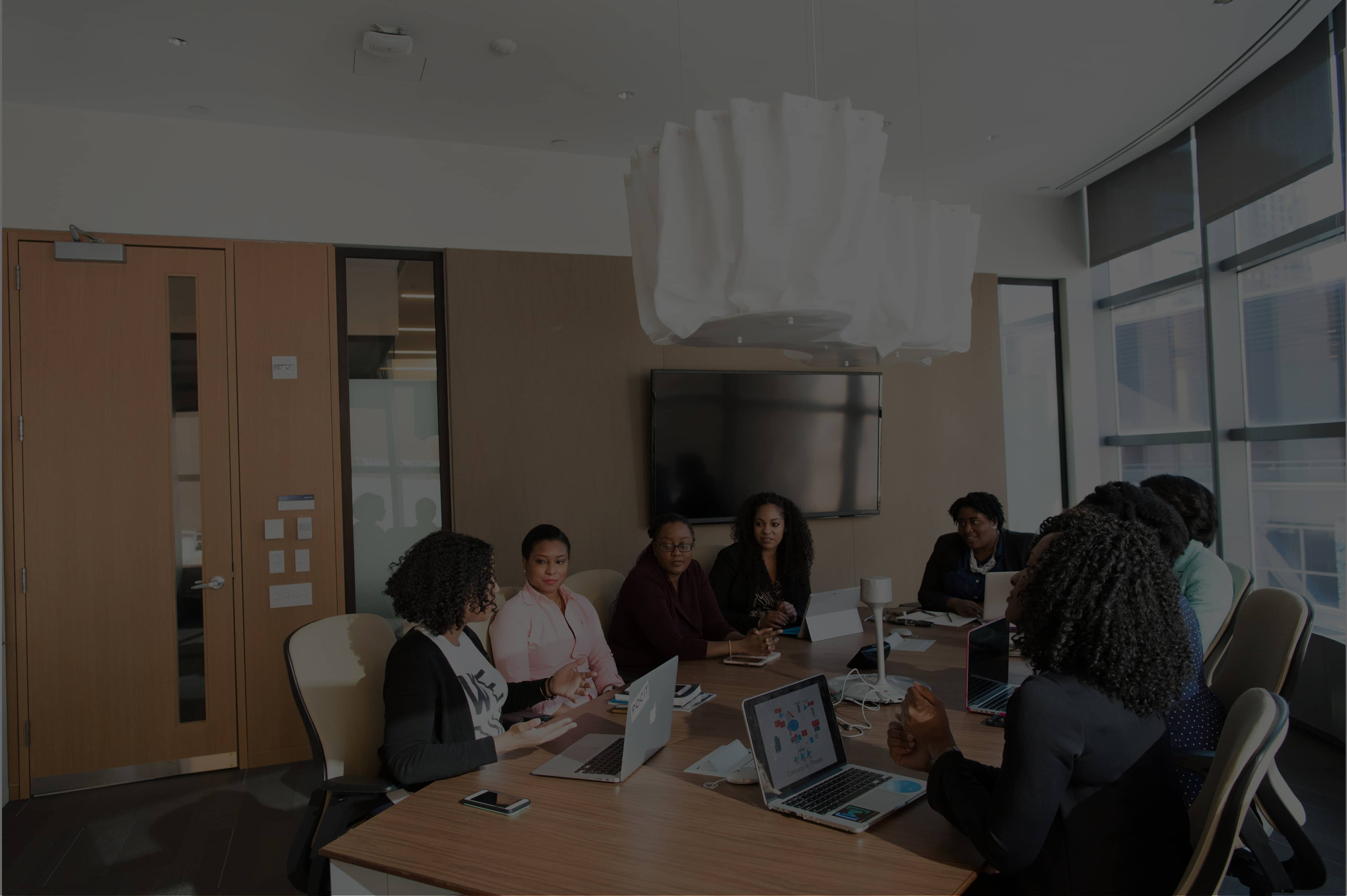 Group of seven people having a meeting around a wooden conference table with laptops in a modern office.
