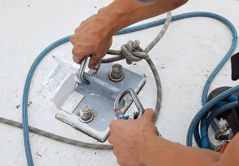 A close-up of a Bax specialist’s hands as tests a roof anchor point that he’s just installed.