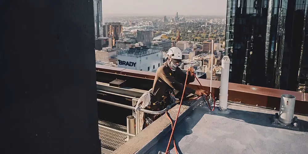 Rope access technician securing safety lines on a high-rise rooftop overlooking the Melbourne CBD, preparing for vertical access work.