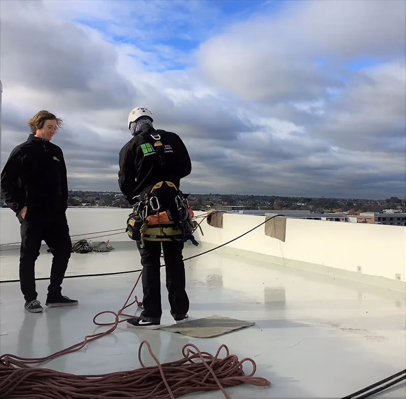 Two workers on a rooftop preparing for high-rise cleaning. 