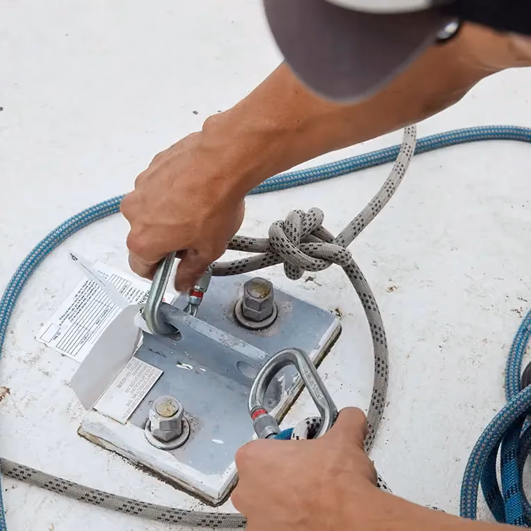 Close-up of a worker’s hands securing safety ropes to a rooftop.
