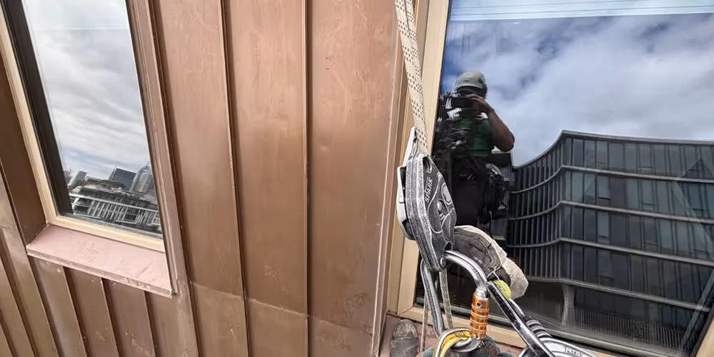 Rope access technician performing a façade inspection on a multi-storey building, with safety gear and ropes visible against reflective windows.