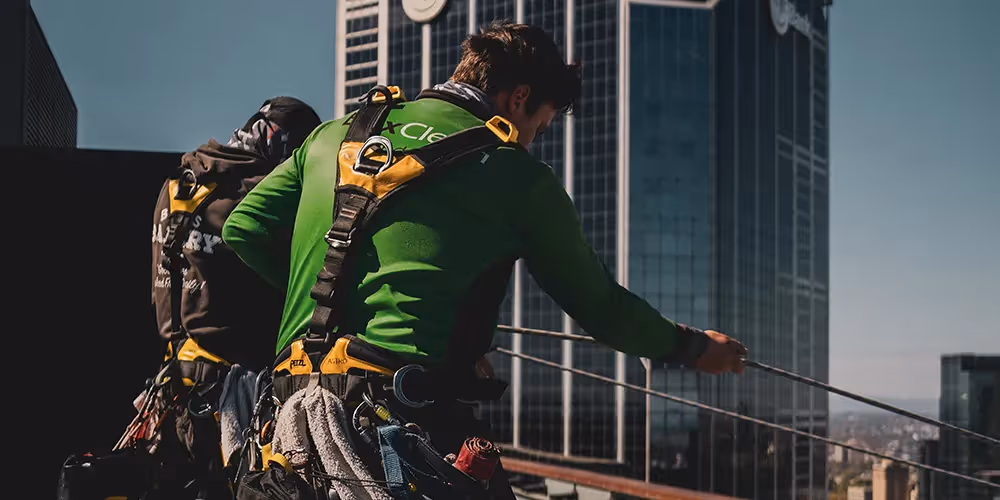 Bax Clean technicians on a rooftop setting up rope access equipment in front of the ME Bank building.