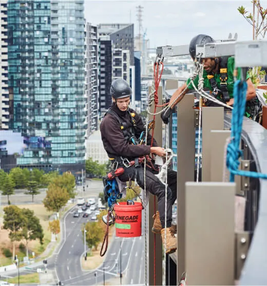 Two rope-access technicians in safety harnesses work on the edge of a high-rise building in Melbourne. 