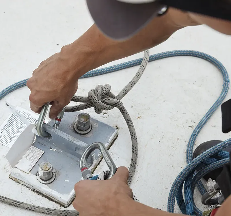Close-up of a worker securing safety ropes to a rooftop. 