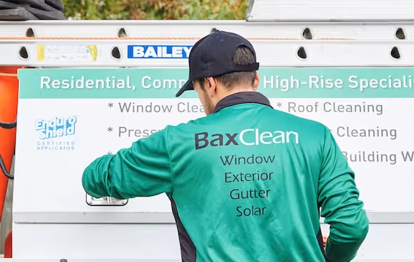 Two high-rise rope-access technicians in harnesses work on the side of a tall building.