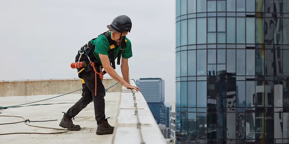 Elevated work platform reaching the top level of an apartment building for exterior maintenance, with a Bax Clean van parked below.