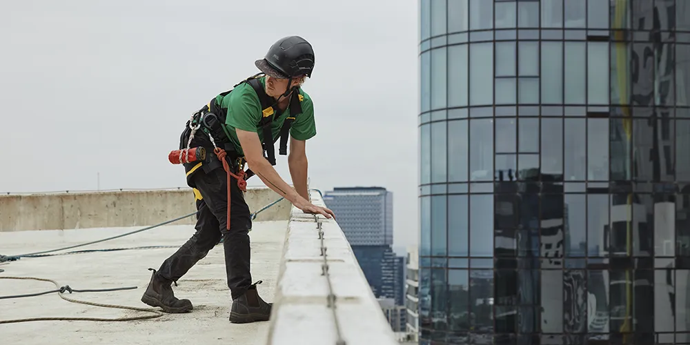 Elevated work platform reaching the top level of an apartment building for exterior maintenance, with a Bax Clean van parked below.