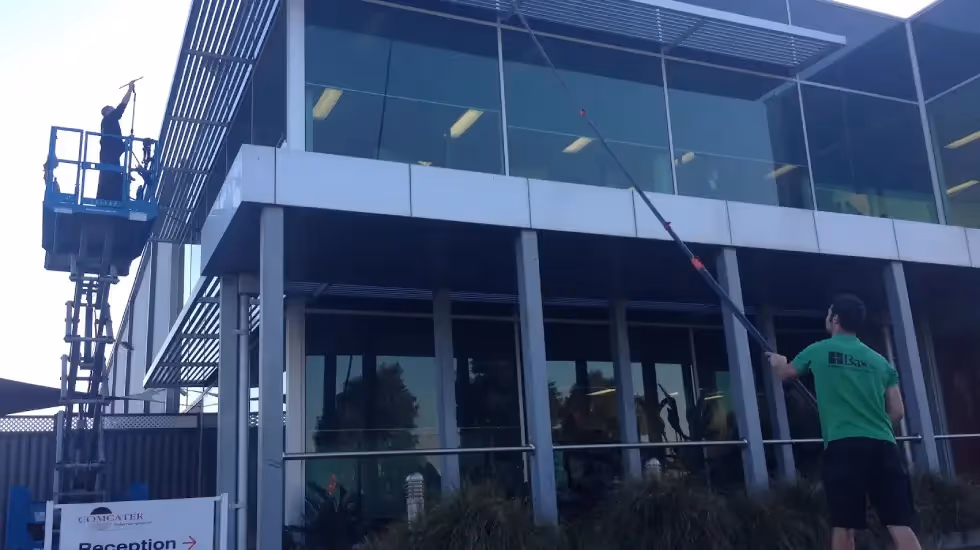 Two Bax Clean workers cleaning large exterior windows of a modern commercial building.