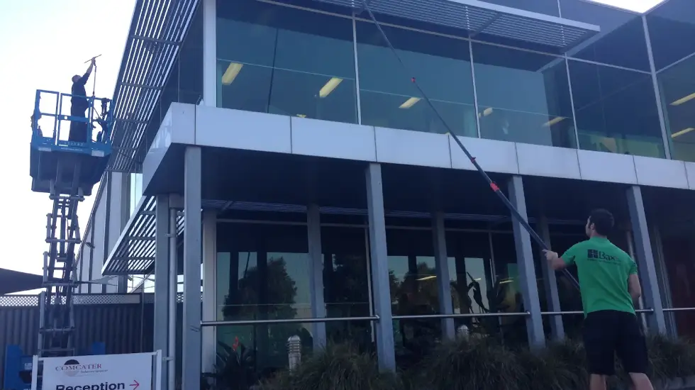 Two Bax Clean workers cleaning large exterior windows of a modern commercial building.