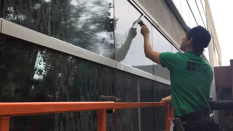 Worker in a green Bax shirt cleaning exterior building windows.