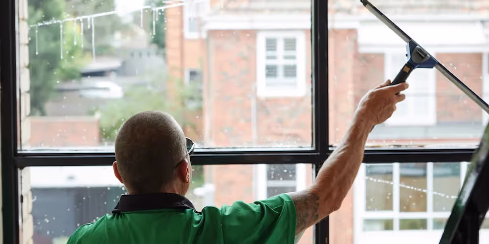 Professional window cleaner removing water and residue from interior glass with a squeegee.