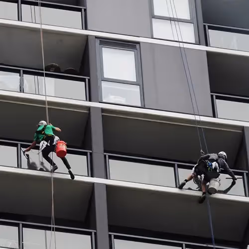 A duo of Bax window cleaners abseiling down the side of an apartment building, secured to roof anchor points we’ve installed for the purpose.