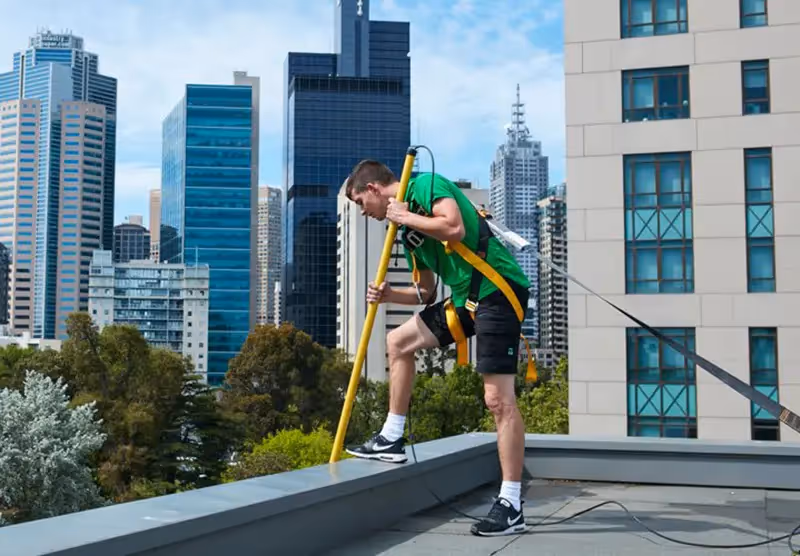 A Bax window cleaner standing at the edge of a rooftop to clean the window below. His harness, attached to a roof anchor point, keeps him perfectly secure.