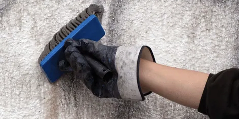 Technician scrubbing graffiti from a textured exterior wall at a Port Melbourne building.