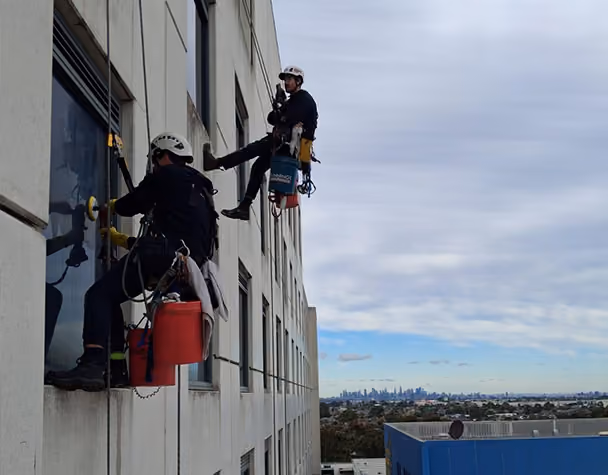 Rope access technician preparing to descend from the rooftop during high-access window cleaning.]