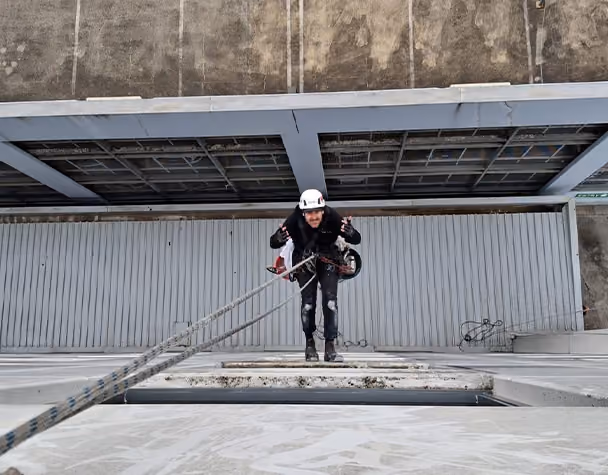 Rope access technician preparing to descend from the rooftop during high-access window cleaning.]