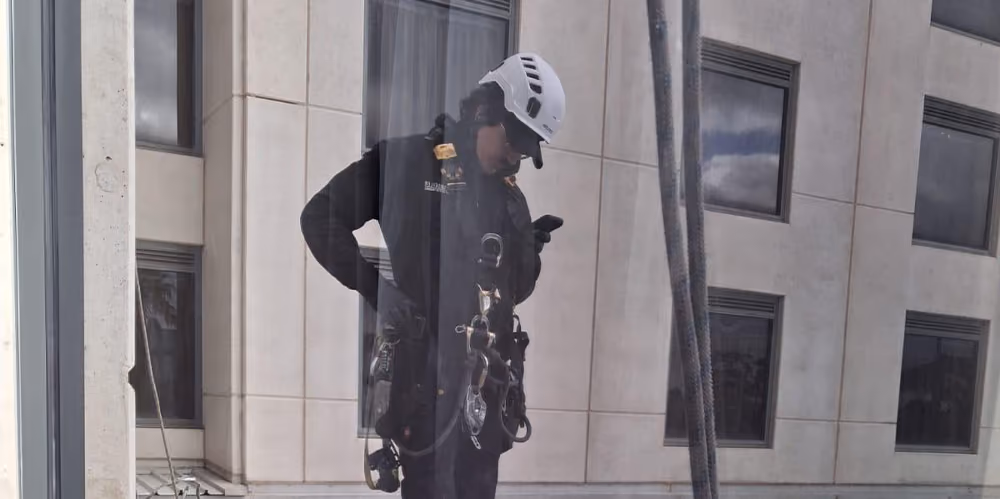Rope access technician standing on the rooftop while preparing equipment for high-access window cleaning.