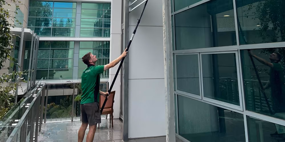 Technician using an extension pole to clean high-level exterior windows at the retirement complex.