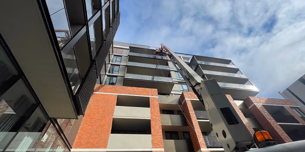 Low-angle view of a boom lift extending to upper floors for high-access exterior glass cleaning.