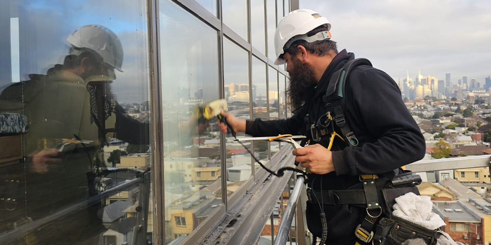 Technician cleaning upper-level exterior windows from an elevated platform at Ardency Kennedy Place.