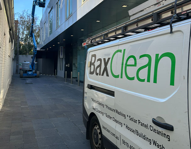 Bax Clean service vehicle parked beside a commercial building while an elevated work platform is used for exterior cleaning.