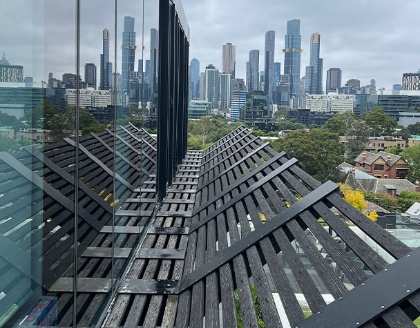 Melbourne skyline reflected in apartment windows above angled timber screening on a South Melbourne residential building.