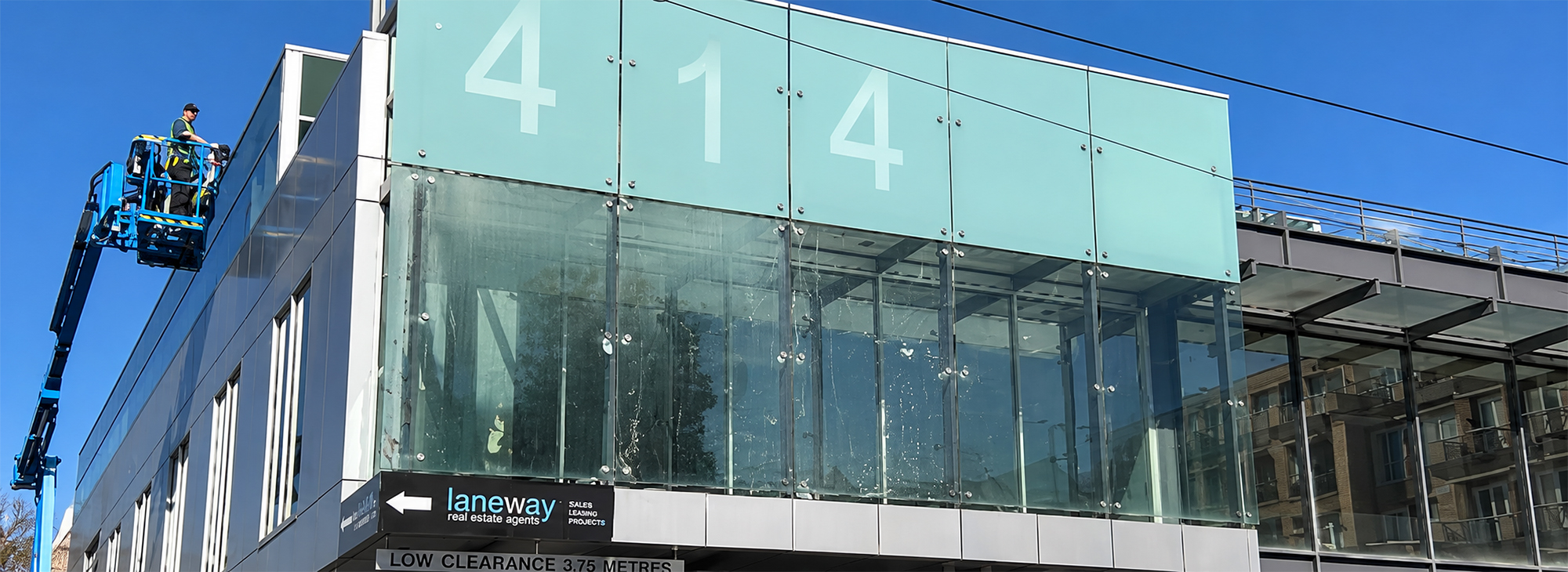 Technician cleaning exterior glass windows beneath a covered walkway at a commercial office building in Toorak.