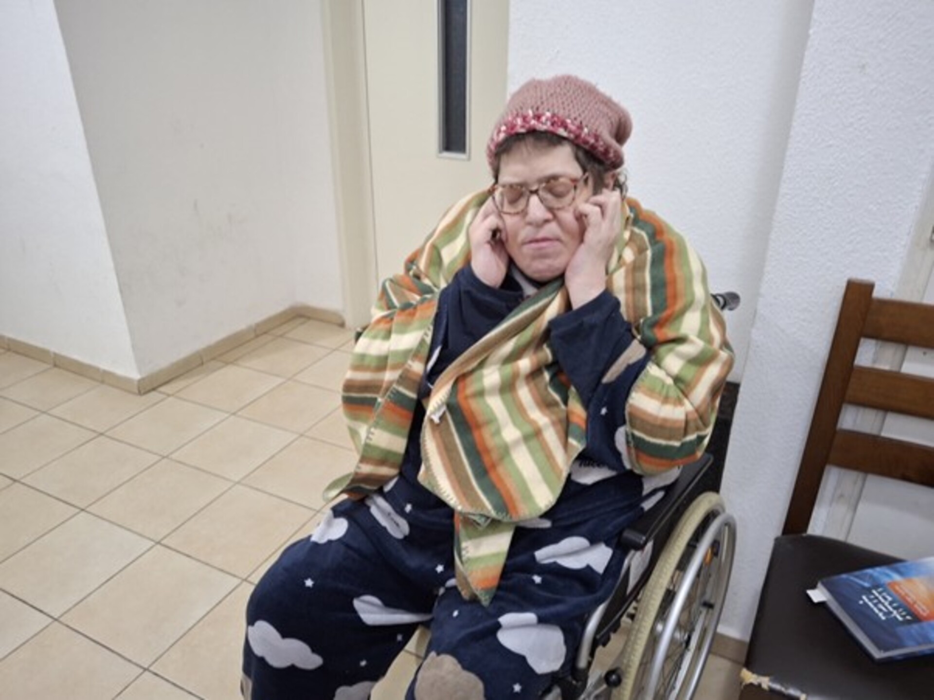 טובית ליפקין עם ידיים על האוזניים, בביתה בפתח תקווה: "אני לא סובלת בומים". צילום באדיבות המצולמת