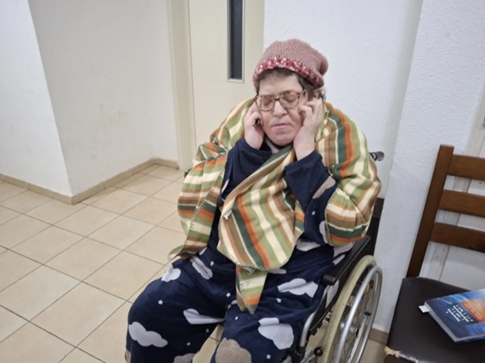טובית ליפקין עם ידיים על האוזניים, בביתה בפתח תקווה: "אני לא סובלת בומים". צילום באדיבות המצולמת