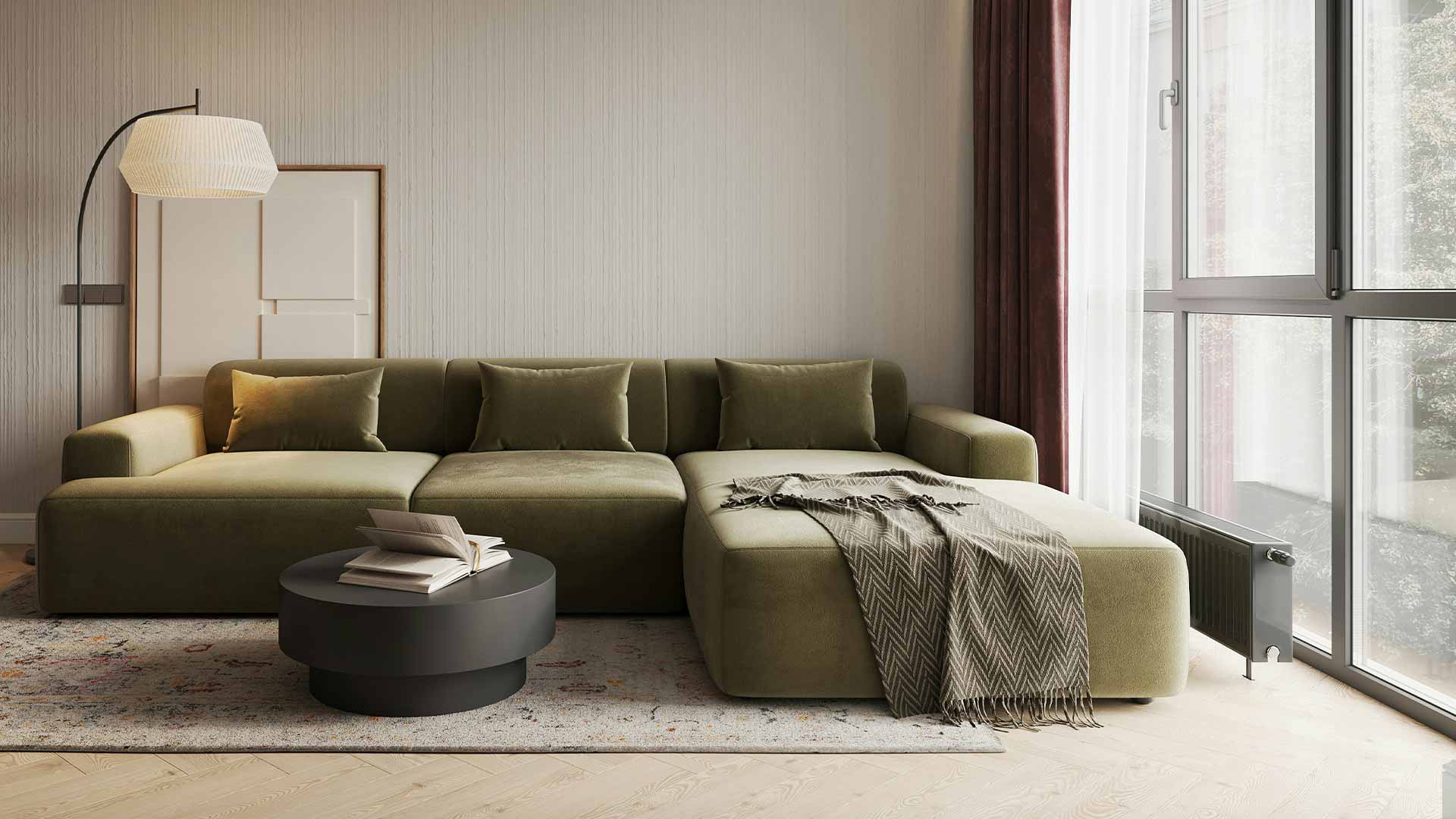 Olive-green corner sofa beside full-height windows, with a round coffee table, floor lamp and textured rug.
