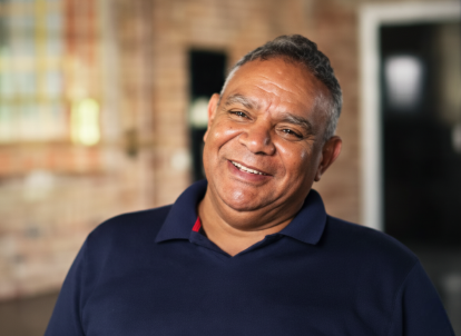 Portrait of Graham from shoulders up wearing a navy shirt and smiling at the camera
