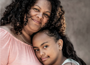 Portrait of Johanna and her daughter from chest up smiling. Johanna is wearing a pink shirt and her daughter is resting her head on Johannas chest 