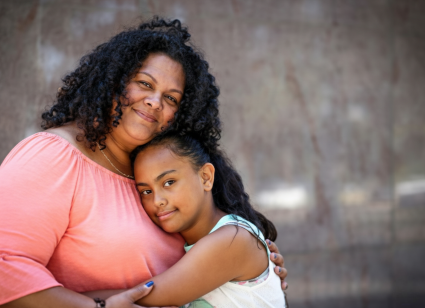 Portrait of Johnna hugging her daughter as they both smile at the camera