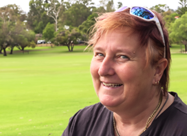 Picture of Tracie outside at a park, sunglasses on her head, smiling at the camera