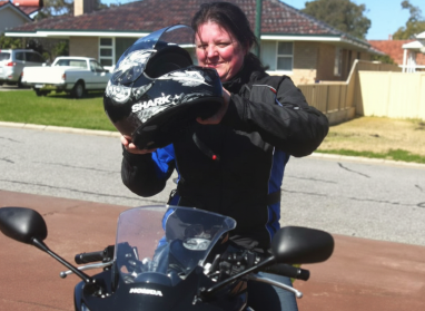 Photo of Liz sitting on her motorbike putting on her helmet