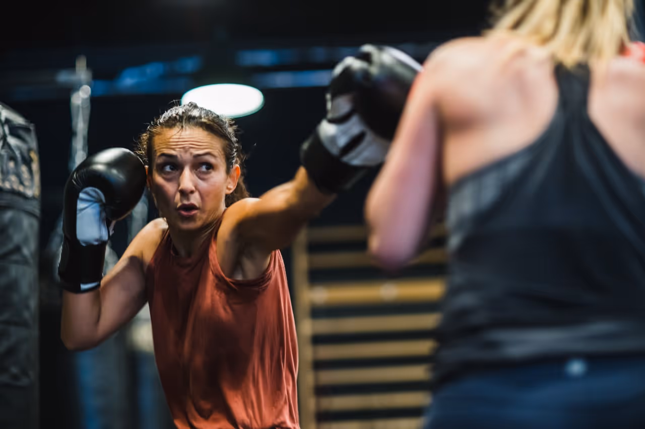 Two women boxing in a gym, one throwing a punch towards the other.