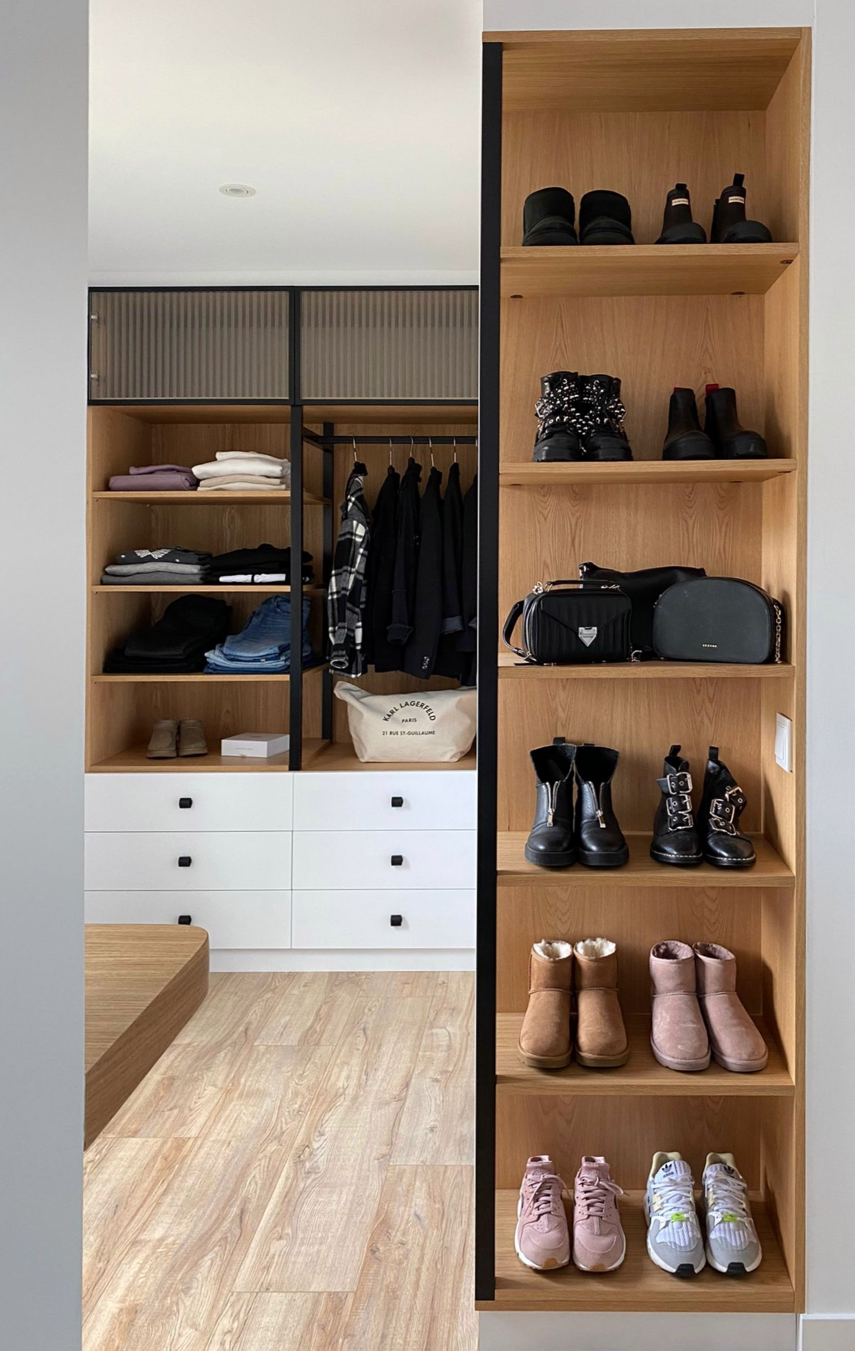 Armario vestidor semi abierto diseñado a medida. Está compuesto por una zona de colgado abierta y otra completamente cerrada. Realizado en color blanco, madera natural de roble y estructura metálica lacada en negro mate.