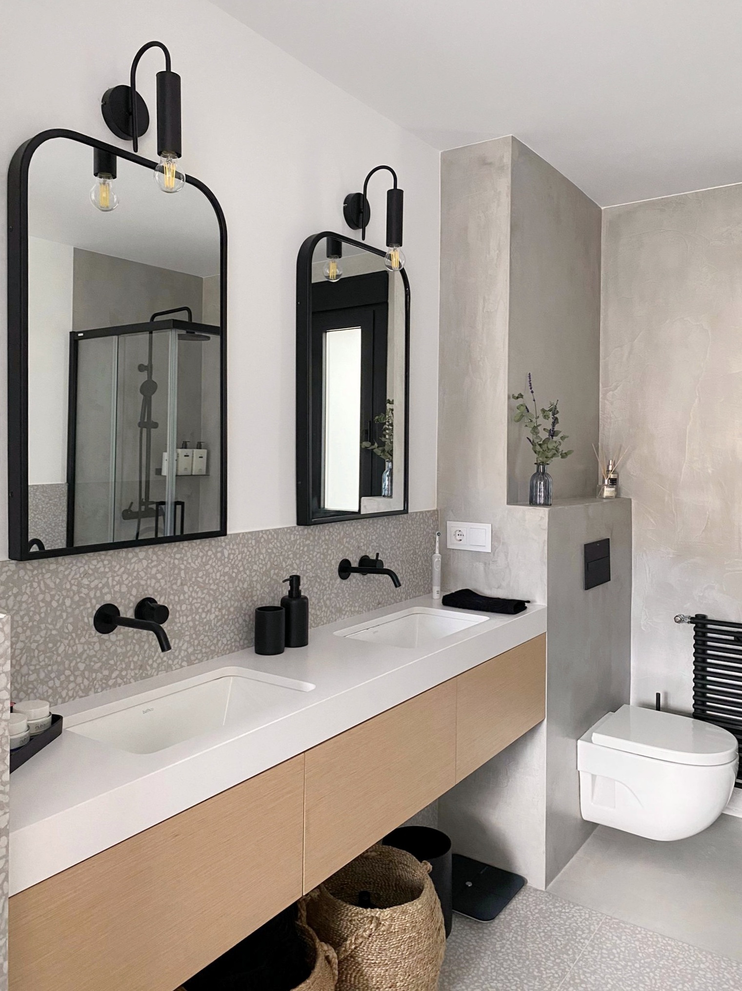 Baño en suite en microcemento y doble lavabo. Mobiliario realizado a medida con cajones en roble natural mate.