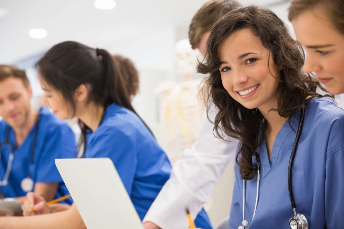 Group of smiling medical students in blue scrubs collaborating during a healthcare training session, representing the BMG Emerging Scholars Program at Gregory Rhodes MD Cancer Center.