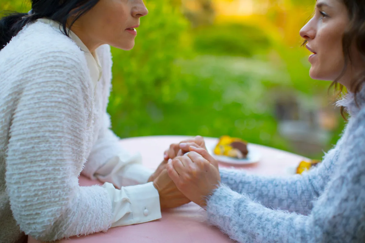 Two women in sweaters hold hands supportively, symbolizing compassion and emotional connection at Gregory Rhodes MD Cancer Center’s Patient Support Services.
