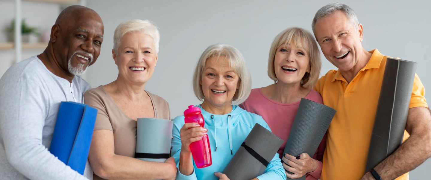 Group of older adults holding yoga mats and smiling, representing improved flexibility and relief from osteoarthritis after receiving Low-Dose Radiation Therapy at Gregory Rhodes MD Cancer Center.