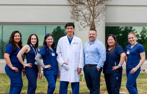 A group of our radiation technicians, an oncology doctor, and cancer center director in front of the Gregory Rhodes MD Cancer Center.