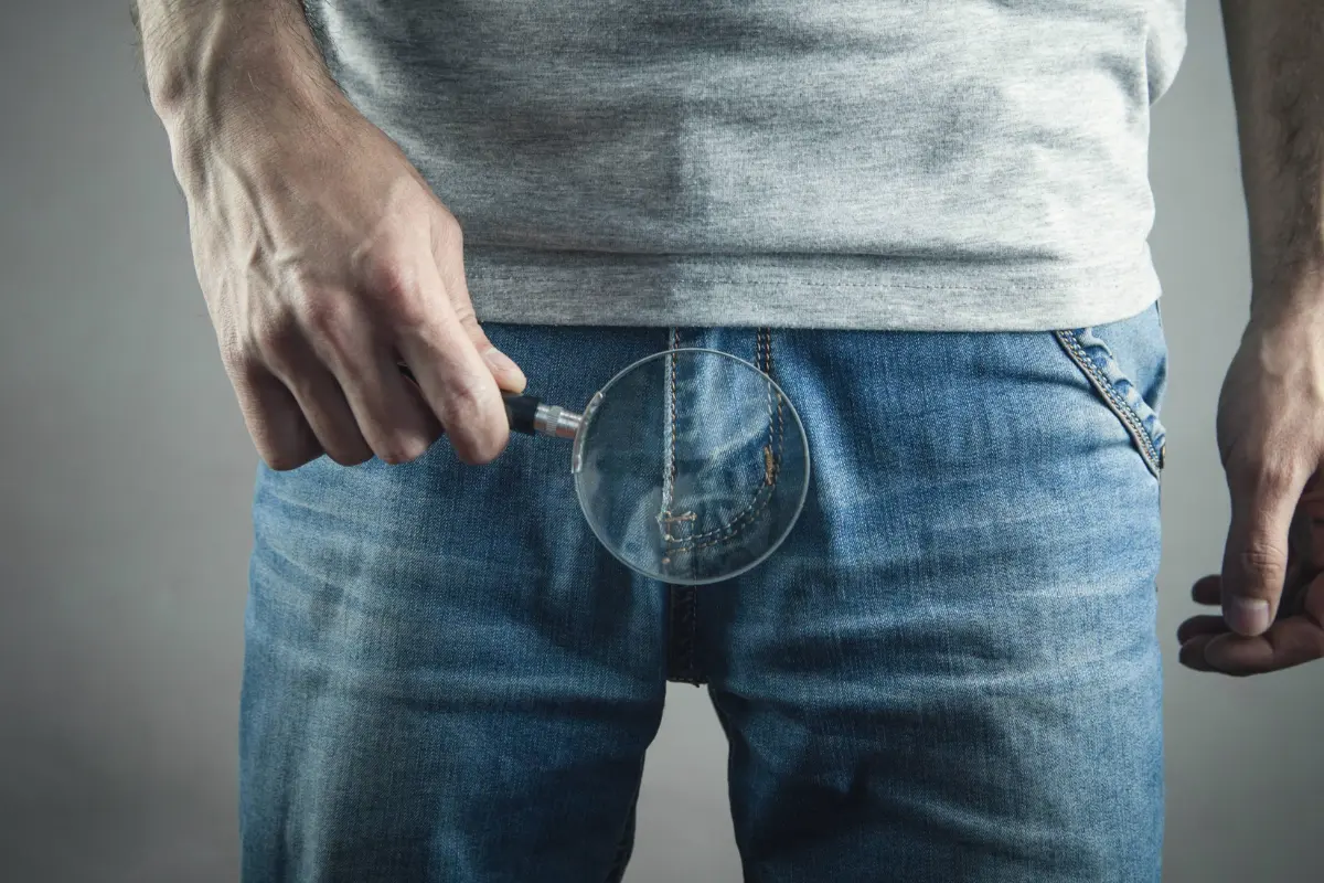 Male patient holding a magnifying glass over his lower abdomen to symbolize prostate health awareness and the importance of early cancer screening.