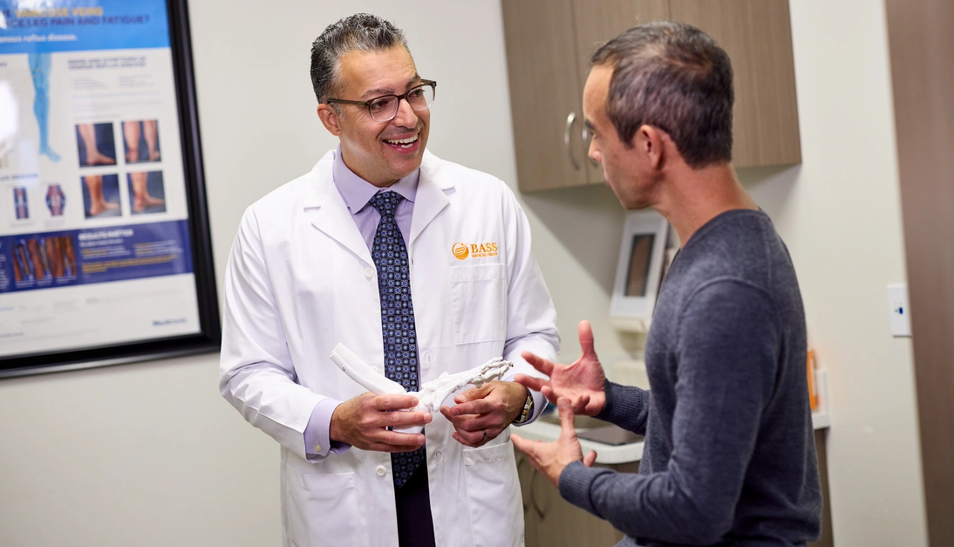 Podiatrist in a white coat holding a foot bone model while explaining to a patient in a consultation room.